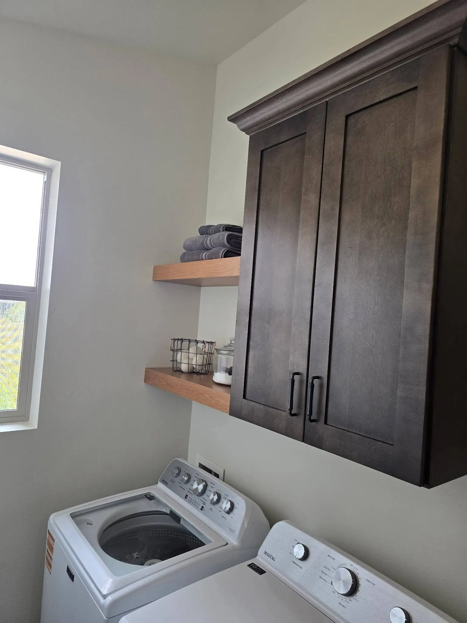 Wall mounted cabinet with floating shelves above a washer and dryer