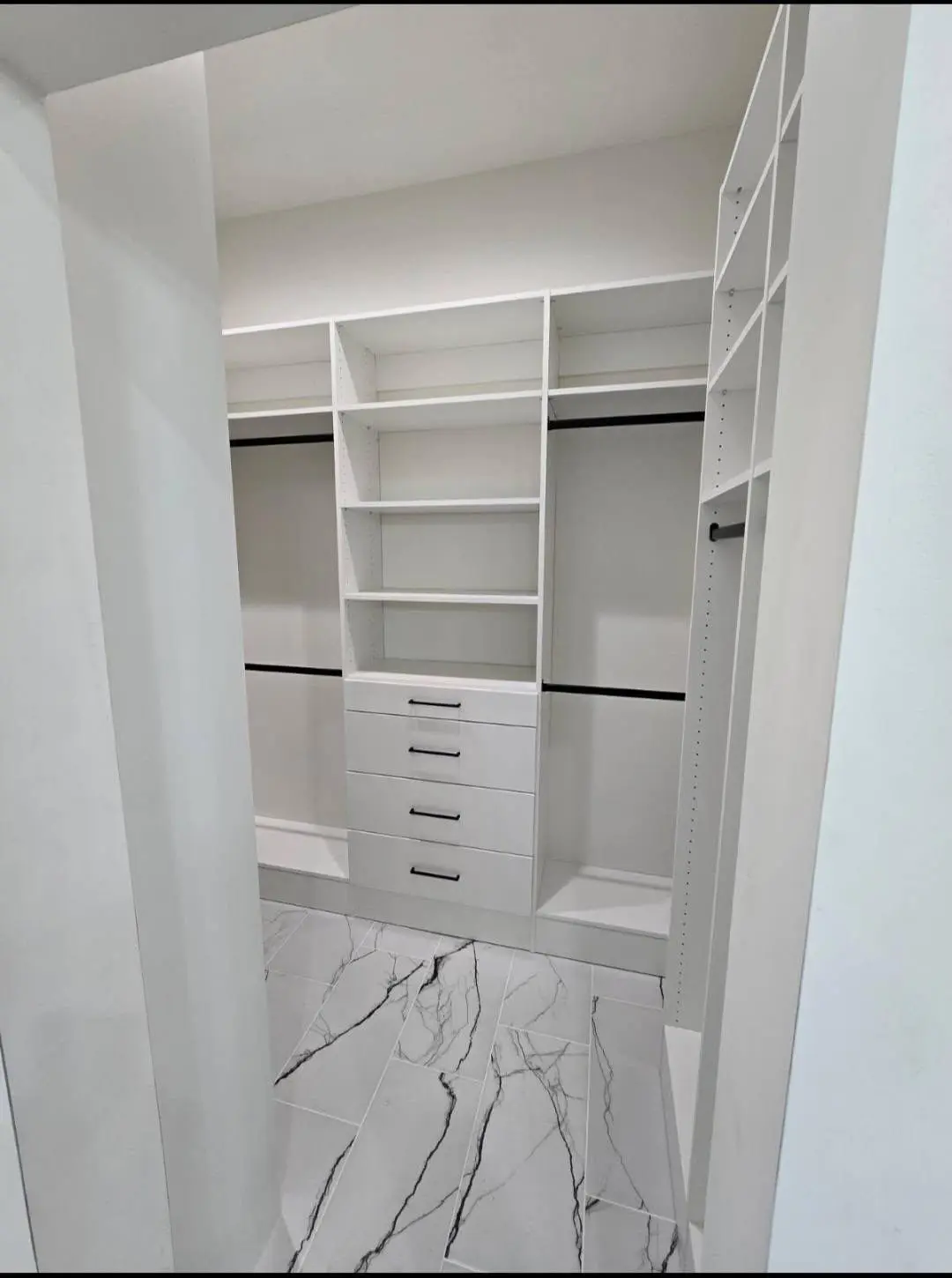 Walk in closet drawers and hanging space over a marble look tile floor